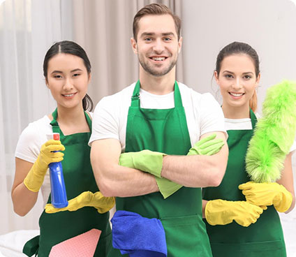 Three people in green aprons and gloves holding cleaning supplies, ready to clean.