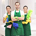 Three smiling cleaners in green aprons holding cleaning supplies.